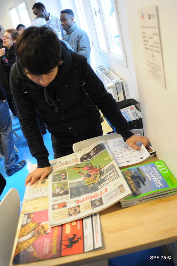 Une personne accompagnée par le Secours populaire lit un journal à l'espace bibliothèque de la Fédération de Paris